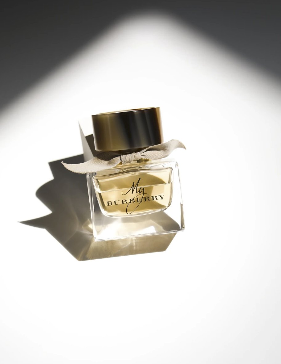 Goldener Parfumflakon mit hartem grafischem Schlagschatten auf Weiß
