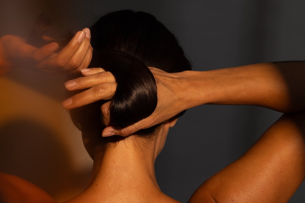 Hände formen einen Haarknoten im Nacken, warmes Streiflicht auf der Haut
