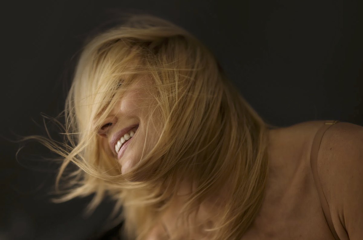 Blonde Frau lacht mit schwingendem Haar im warmen Licht