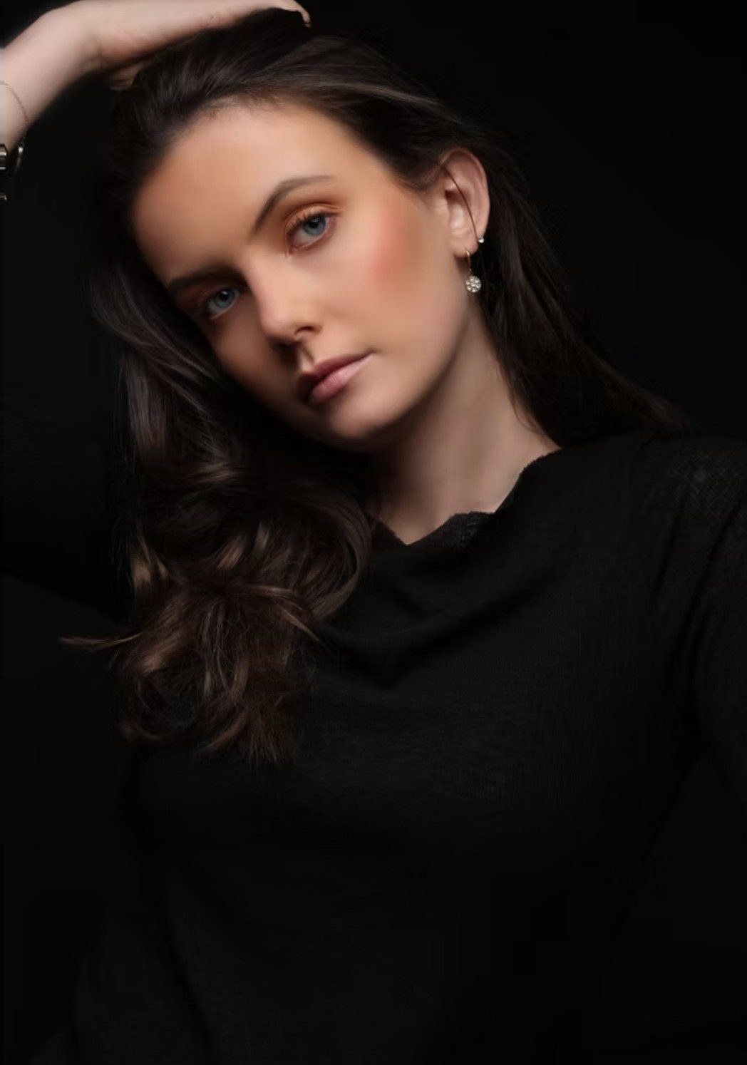 Junge Frau mit gewelltem Haar in schwarzem Oberteil im Low-Key-Beautyportrait