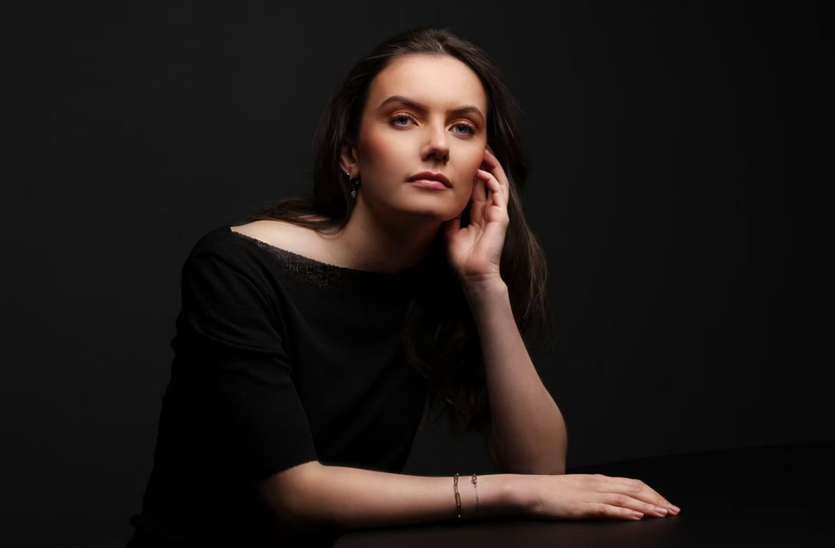 Dunkelhaarige Frau stützt den Kopf auf und blickt in die Kamera, Low-Key-Studioportrait