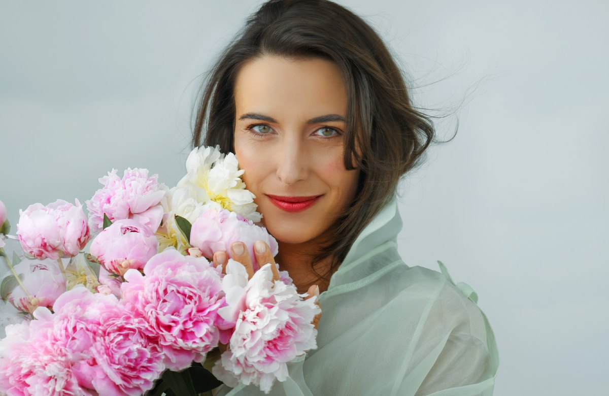 Frau in mintfarbener Bluse hält einen Strauss rosa Pfingstrosen