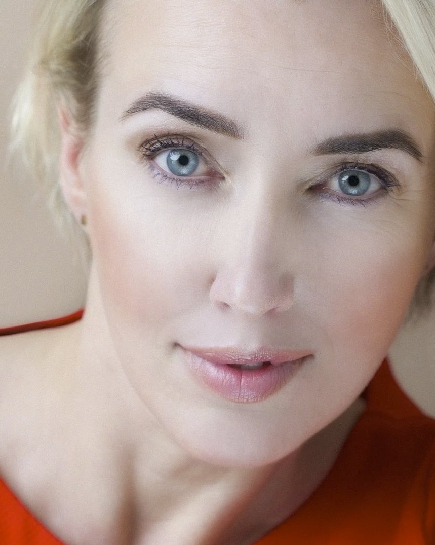 Nahes Beautyportrait einer blonden Frau mit blauen Augen in orangefarbenem Top