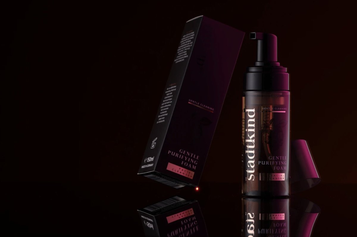 Stadtkind Gentle Purifying Foam Pumpflasche neben ihrer Verpackung auf spiegelnder Fläche vor dunklem Hintergrund