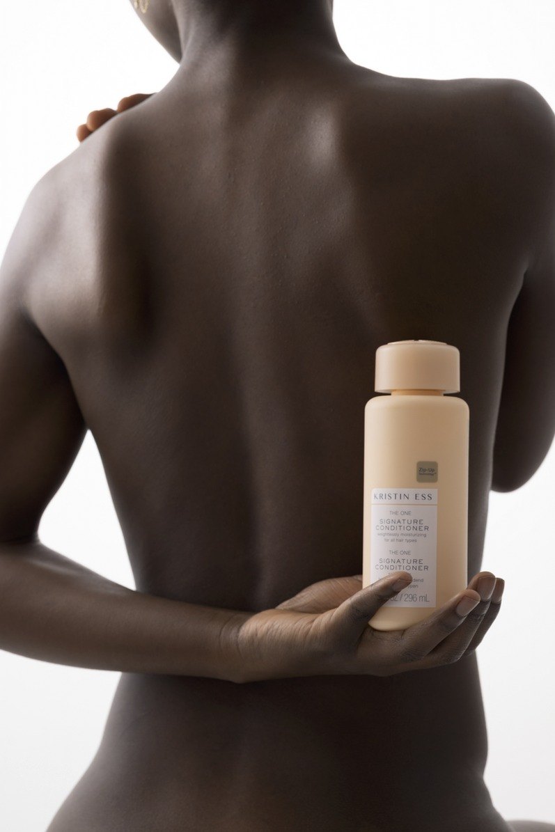 Rücken einer Frau, die vor dem Körper eine cremefarbene Kristin Ess Conditioner Flasche hält