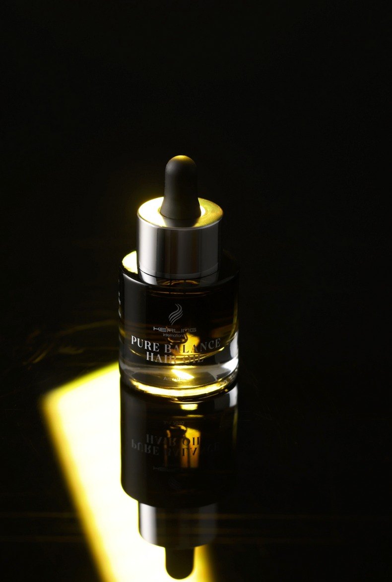 Dunkle Pure Balance Hair Oil Pipettenflasche in einem schmalen goldgelben Lichtstreifen vor schwarzem Hintergrund