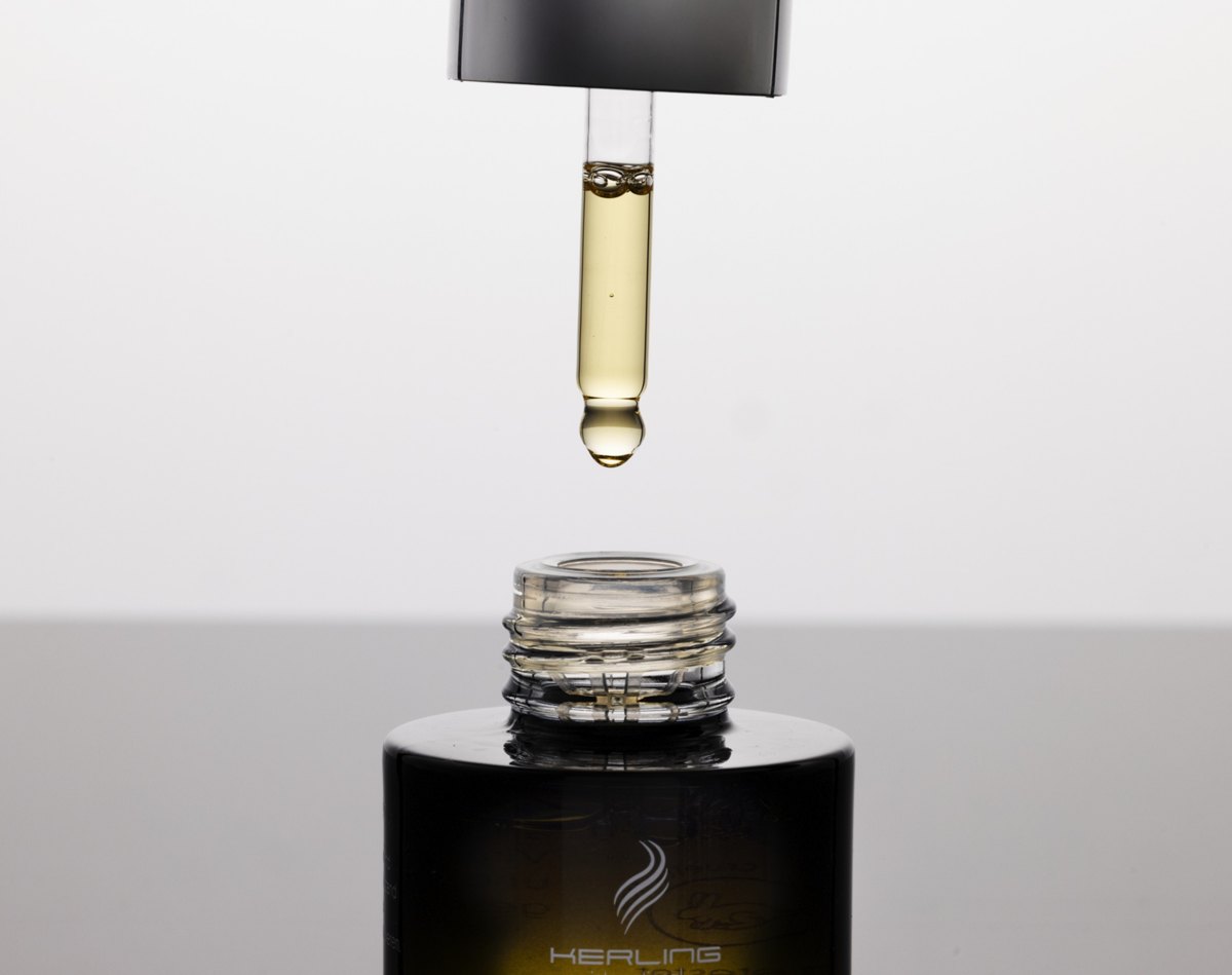 Goldgelber Öltropfen hängt an einer Pipette über der geöffneten Kerling Hair Oil Flasche