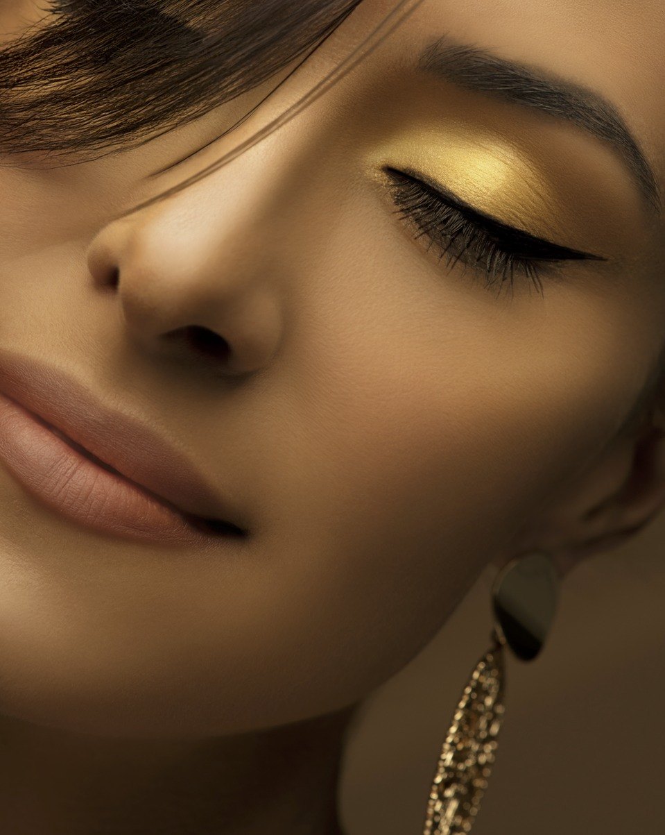 Beauty-Nahaufnahme eines Gesichts mit goldenem Lidschatten, schwarzem Eyeliner und glitzerndem Ohrgehänge