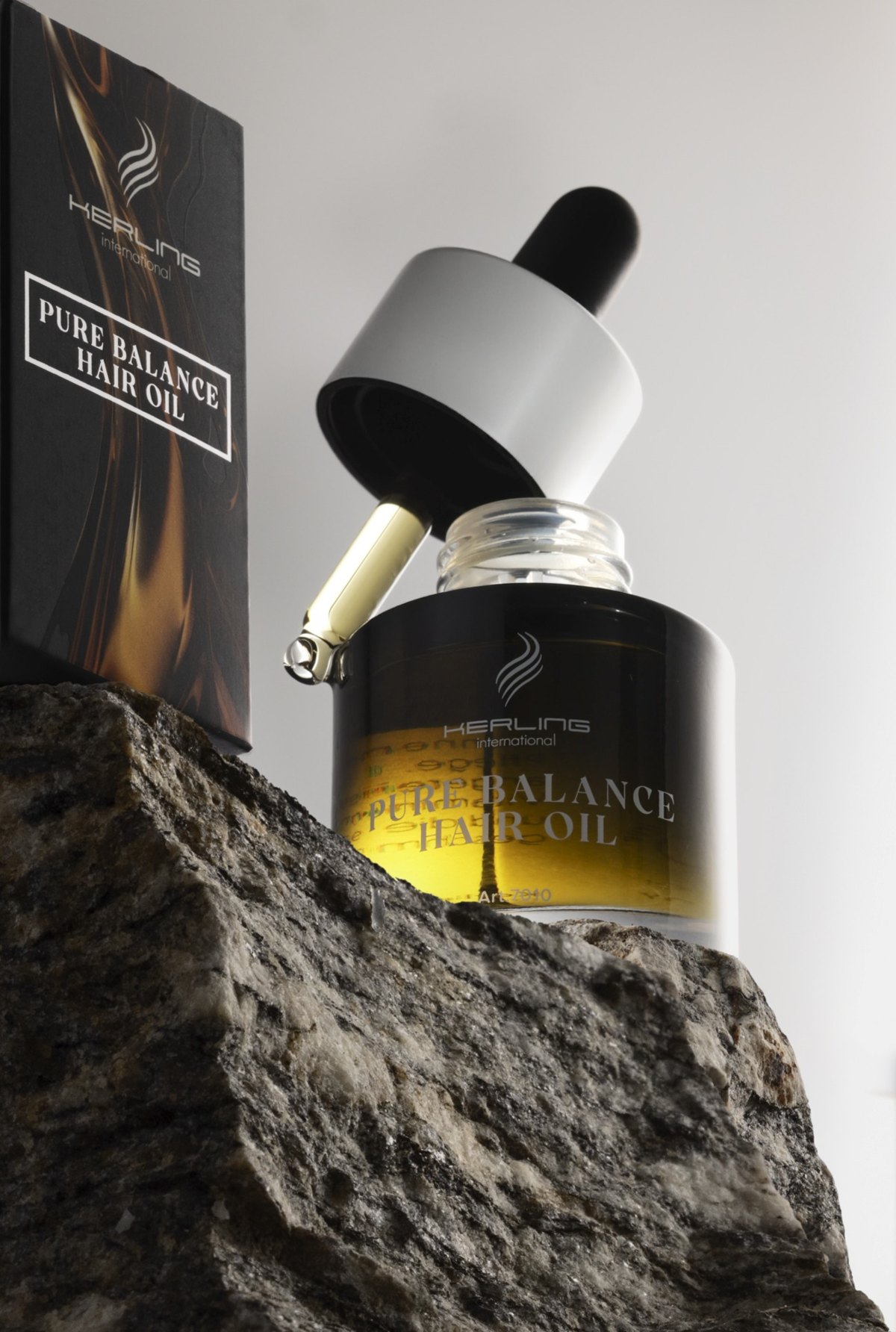 Kerling Pure Balance Hair Oil Flasche mit goldenem Öl auf rohem Steinblock neben der Verpackung