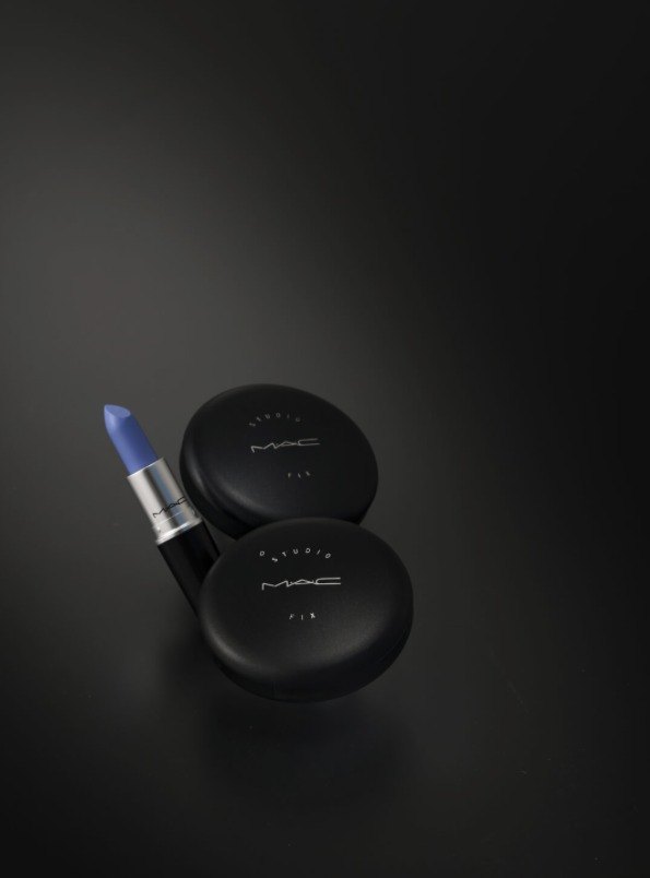 Blauer MAC Lippenstift und zwei schwarze MAC Studio Fix Puderdosen auf dunkler Fläche