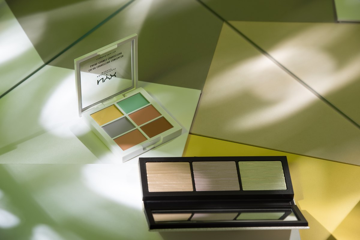 NYX Color Concealer Palette und eine Highlighter-Palette auf grün gefiltertem Untergrund im Blattschatten