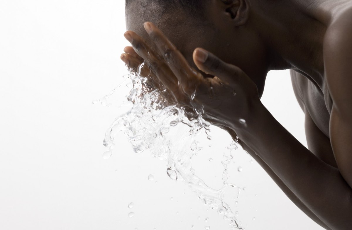 Mann mit dunkler Haut beugt sich vor und spritzt sich mit beiden Händen Wasser ins Gesicht