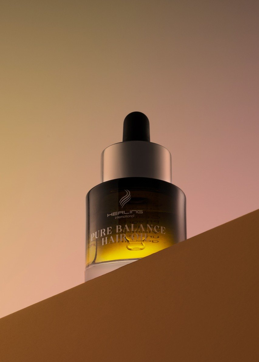 Kerling Pure Balance Hair Oil Flasche auf einer Kante vor pastelligem Rosa-Beige-Verlauf von unten fotografiert