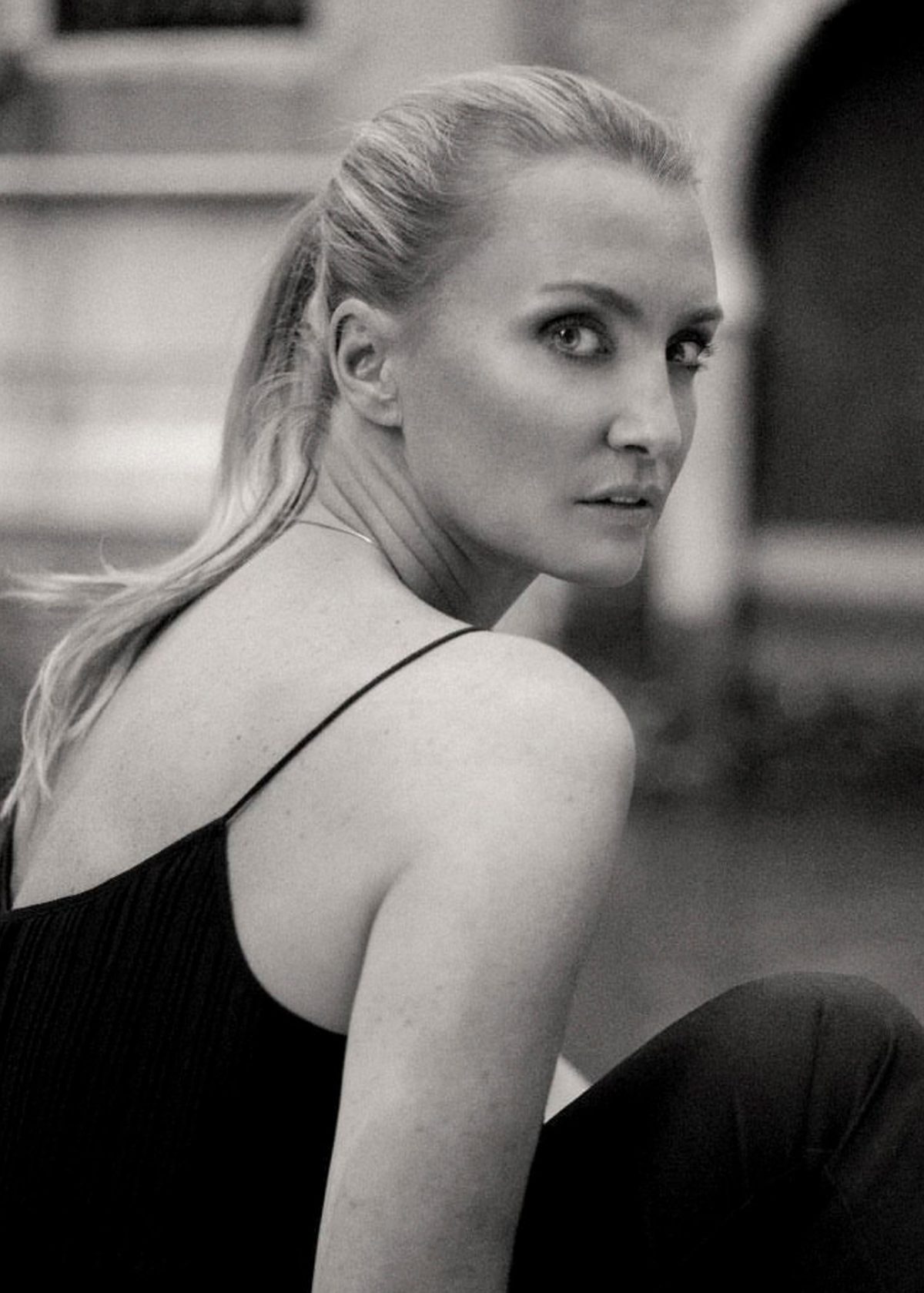 Schwarzweisses Modeportrait einer blonden Frau im schwarzen Trägertop mit Blick über die Schulter