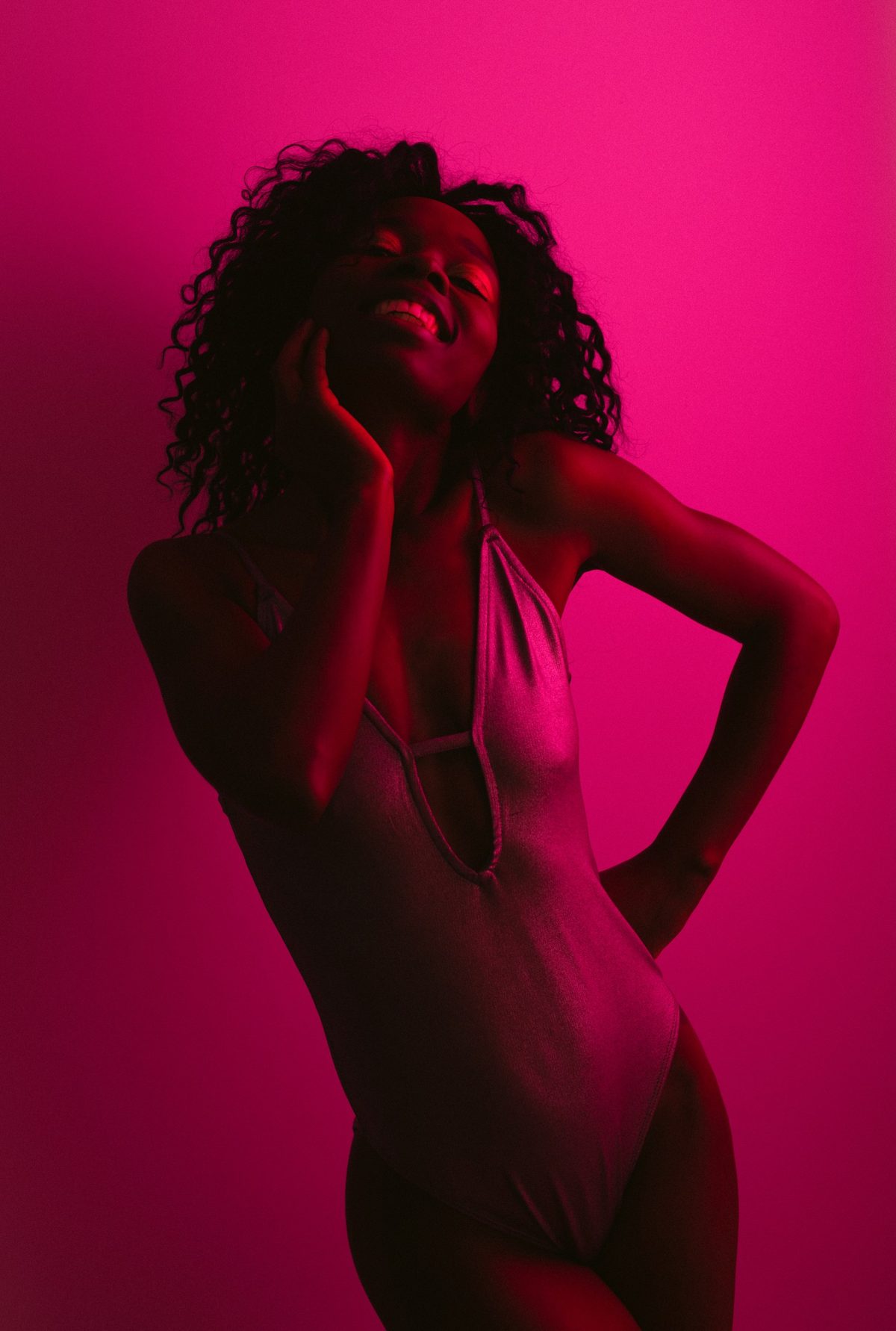 Lachendes Model im Bodysuit vor pinkfarbenem Studiohintergrund in monochromem Farblicht