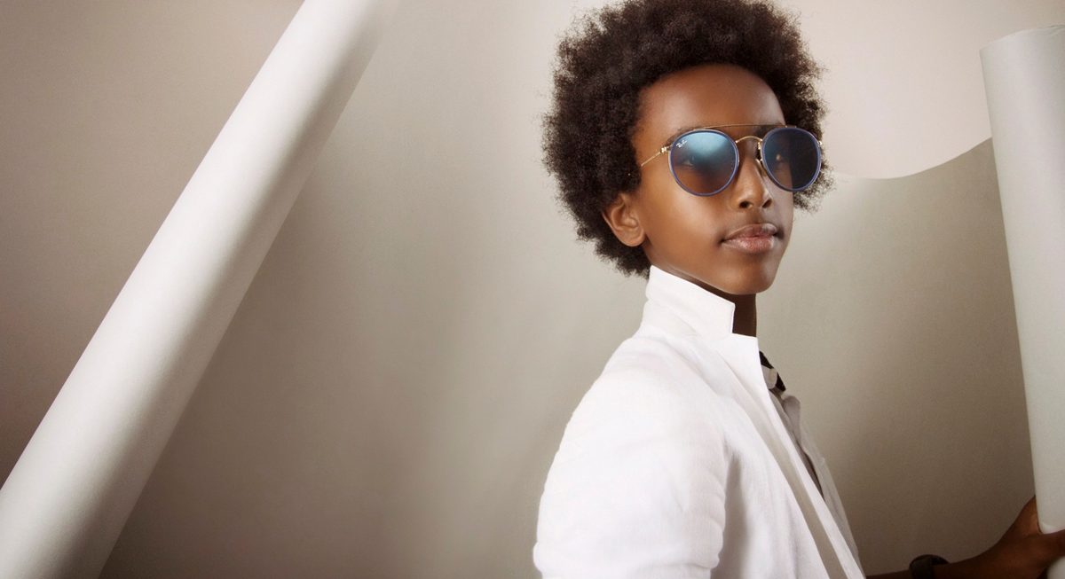 Kind mit verspiegelter Sonnenbrille und weißem Hemd zwischen Papierbahnen im Studio