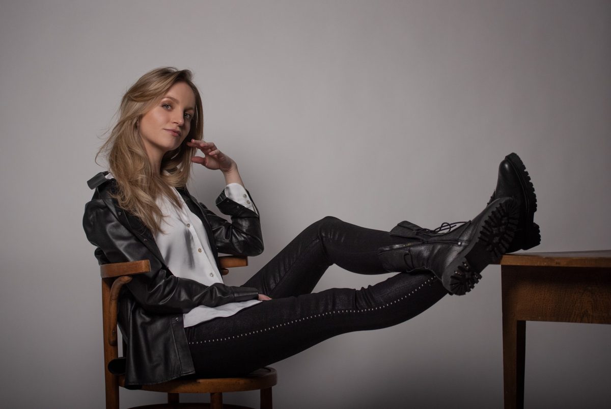 Blonde Frau in Lederjacke und Boots sitzt auf einem Stuhl mit Beinen auf dem Tisch