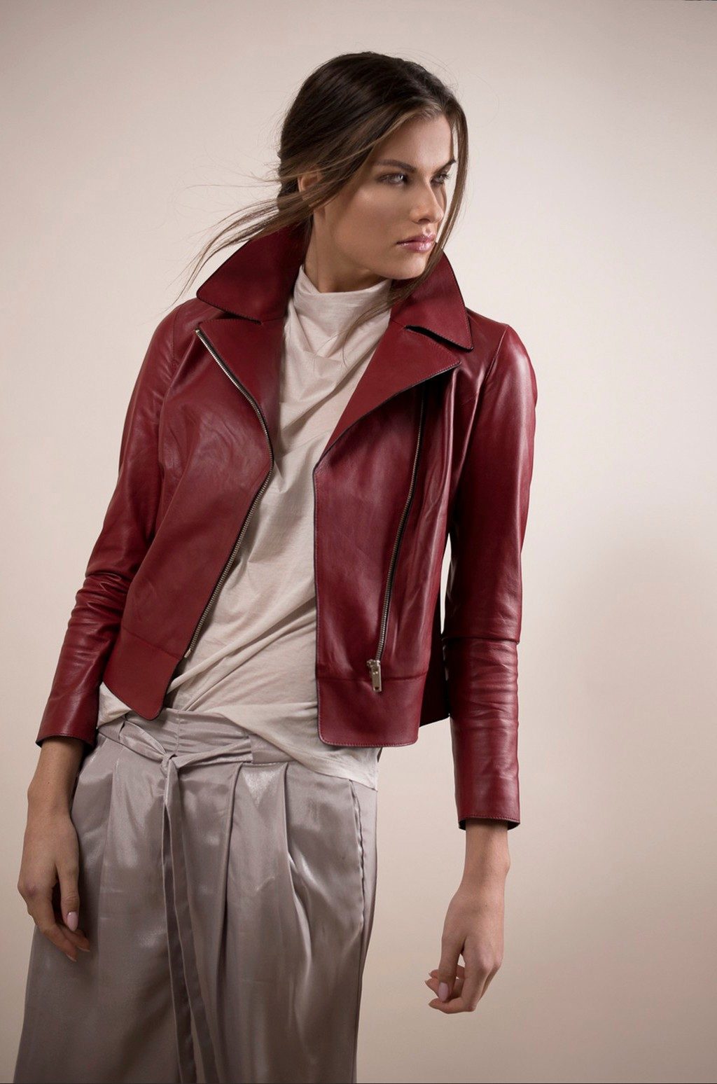 Model in dunkelroter Lederjacke und glänzender Hose vor beigem Studiohintergrund