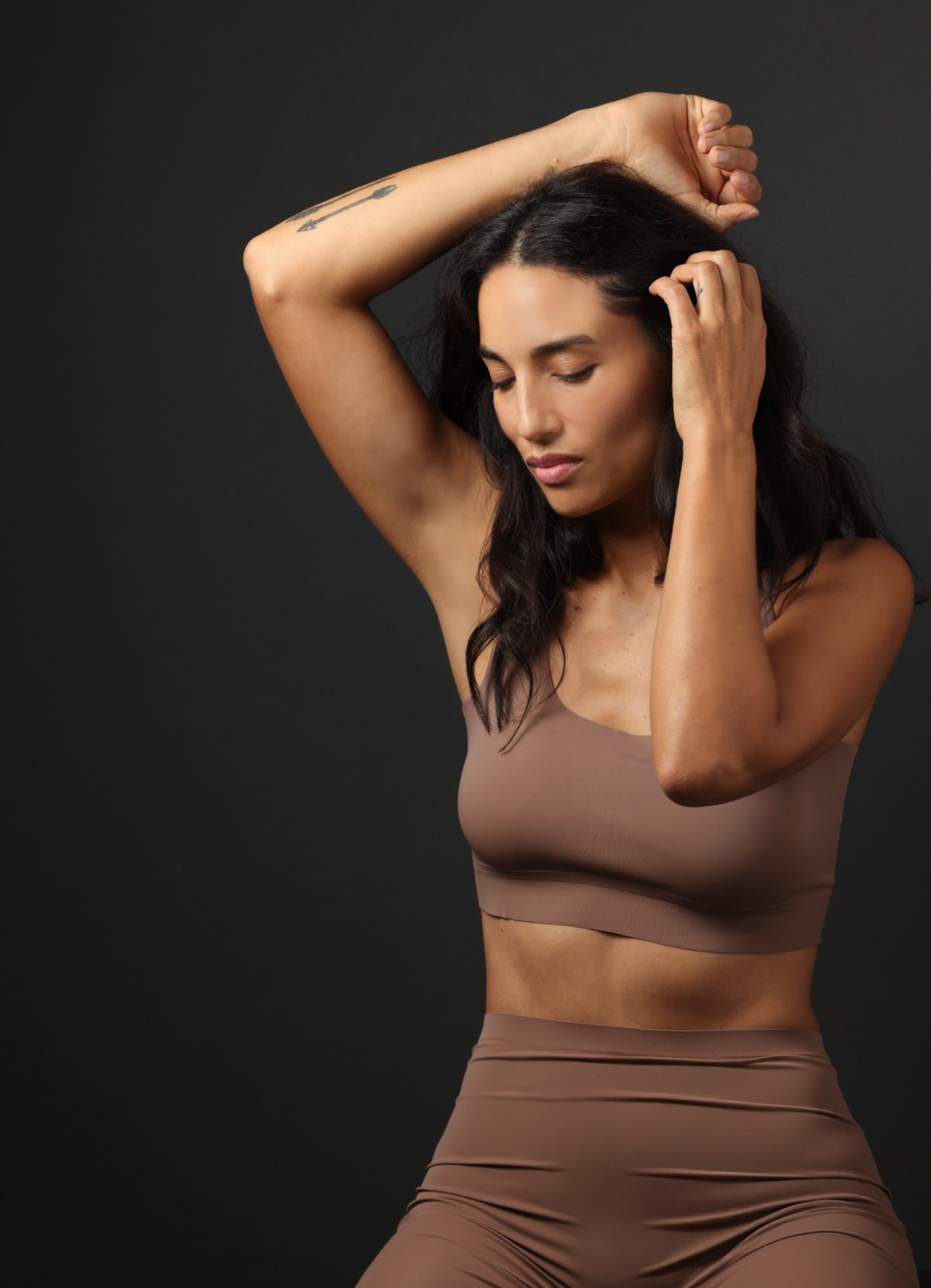 Model in nudefarbenem Sport-Set aus Bustier und Leggings vor dunkelgrauem Studiohintergrund