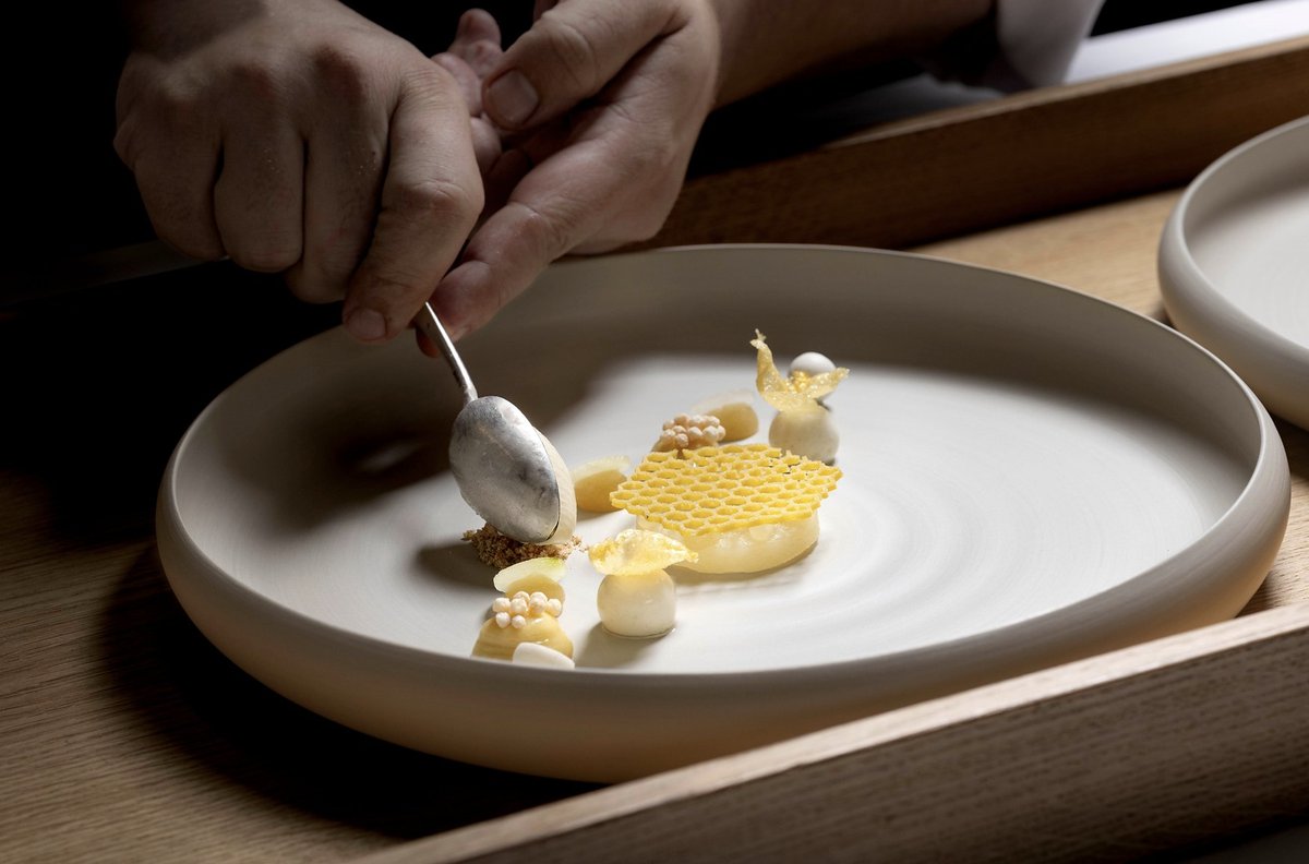 Koch richtet ein helles Dessert mit Wabengitter auf einem tiefen Keramikteller an