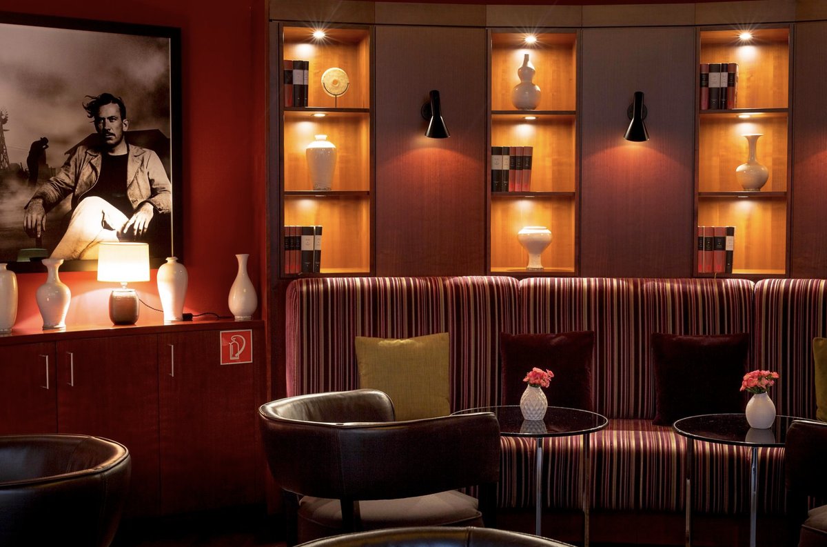 Hotelbar-Lounge mit gestreiftem Samtsofa, Ledersesseln und beleuchteten Wandnischen mit Vasen und Büchern