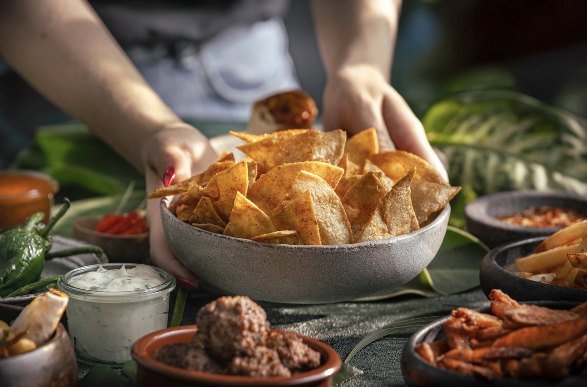Hände stellen eine Schale mit Nachos auf einen Tisch voller Tapas, Dips und Pommes