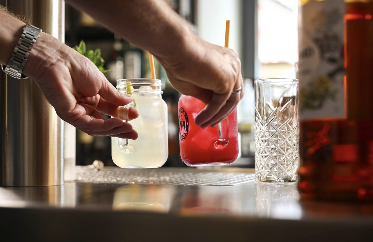 Barkeeper stellt zwei Drinks in Henkelgläsern von Ruffs Burger auf die Bartheke