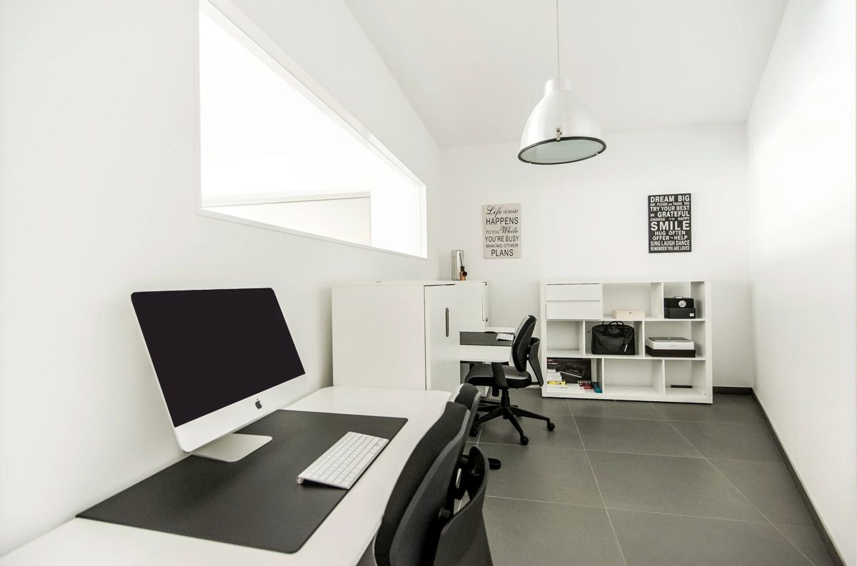 Kleines weißes Büro mit Schreibtisch, Monitor, Drehstühlen und Regal