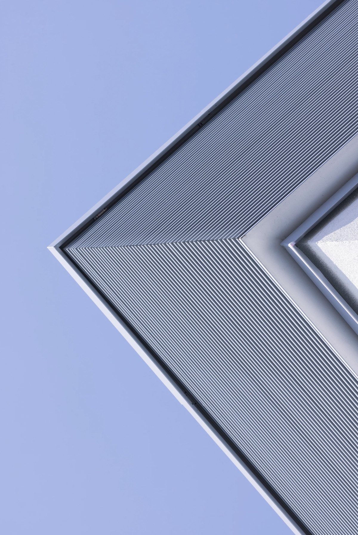 Grafische Gebäudeecke mit feiner Lamellenfassade vor hellblauem Himmel