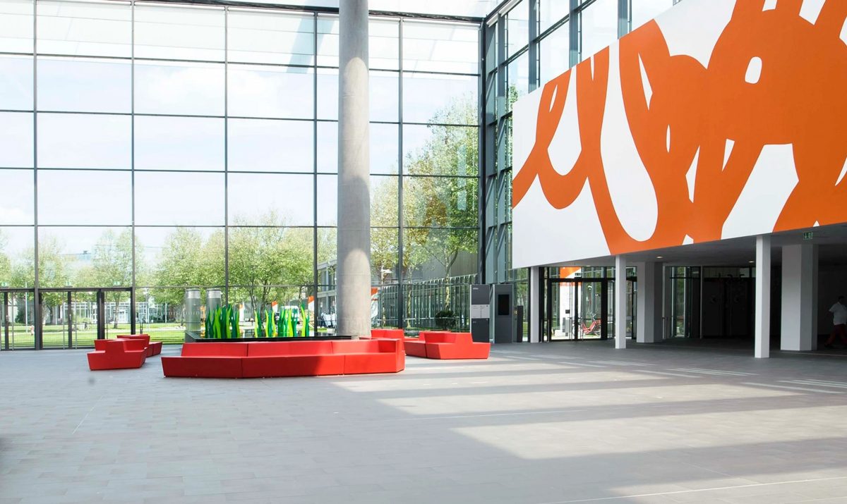 Helles Foyer mit roten Sitzinseln, Glasfassade und großem orangefarbenem Wandbild