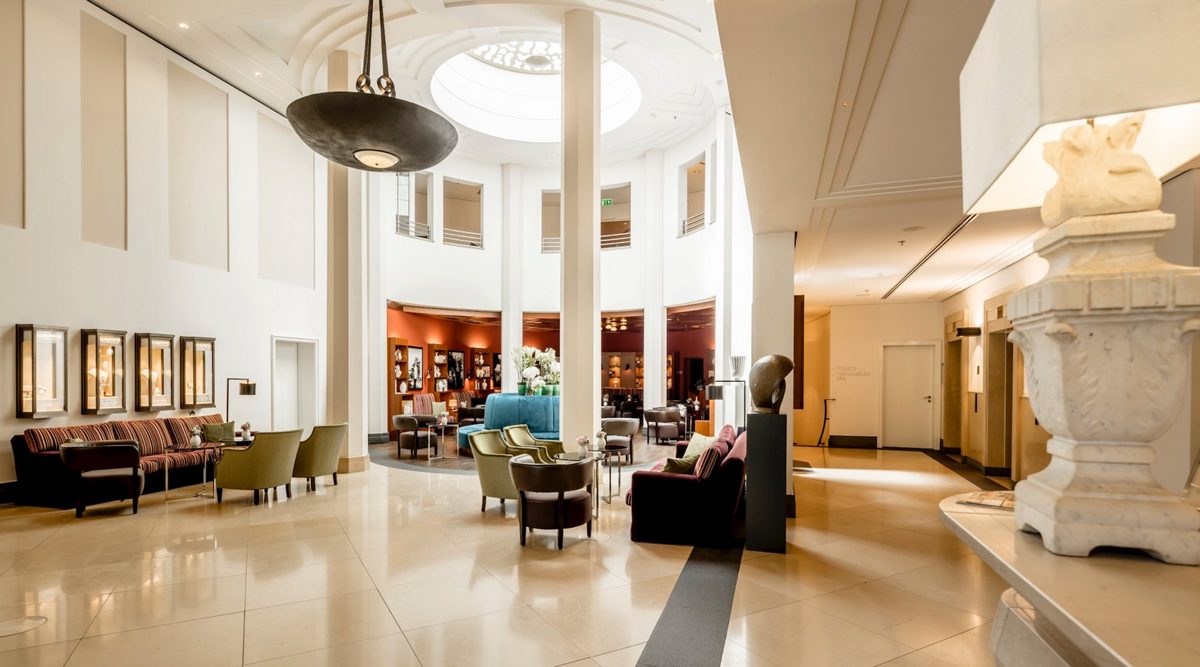 Helle Hotellobby mit weißen Säulen, Oberlicht und farbigen Sitzgruppen
