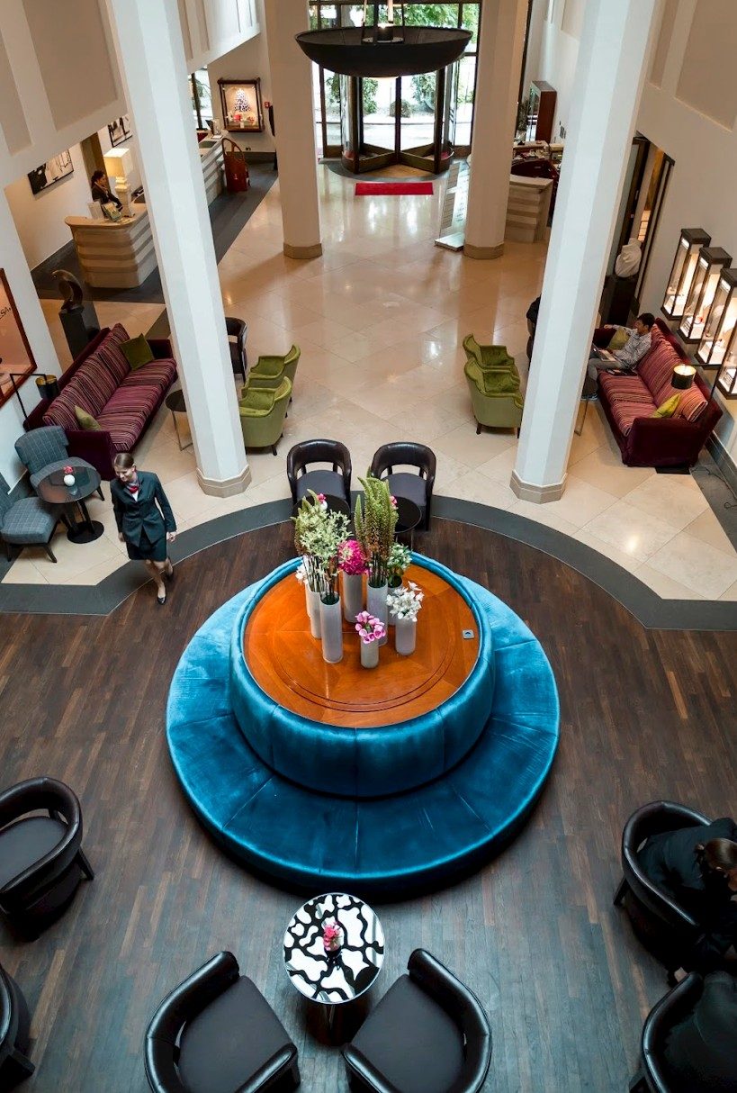Hotellobby von oben mit runder türkisfarbener Sitzbank und Blumenarrangement