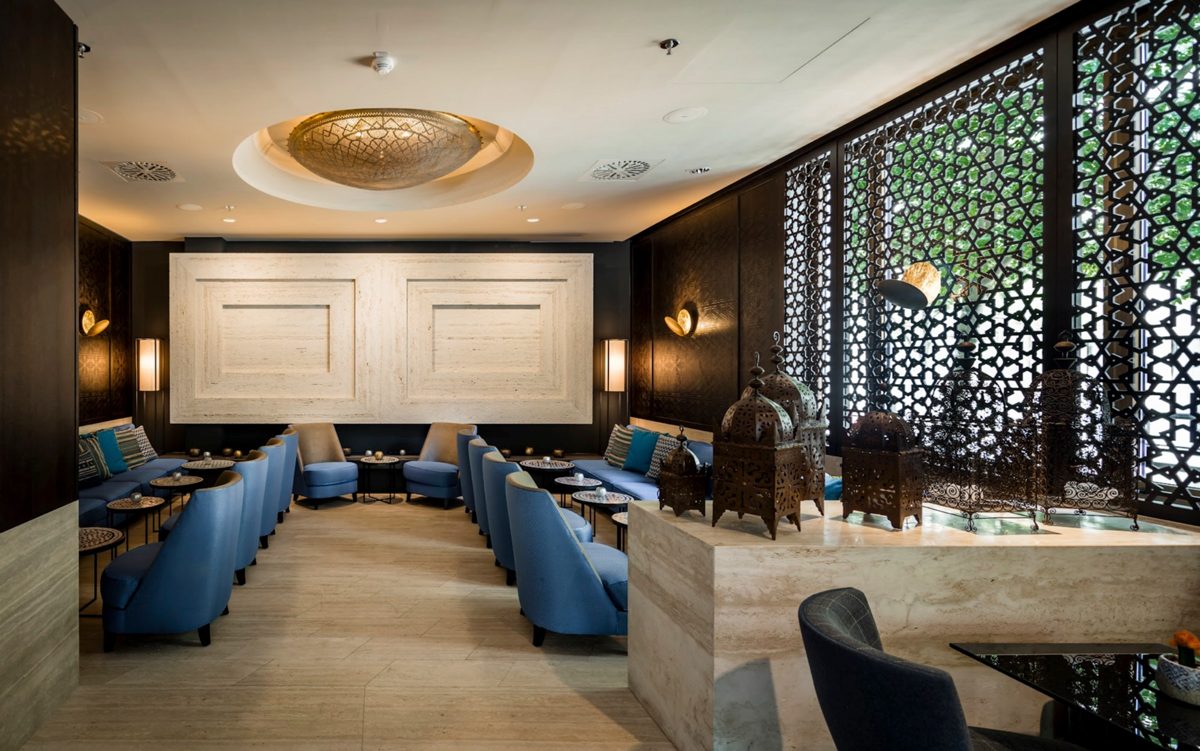 Hotellounge mit blauen Sesseln, ornamentalen Gitterwänden und goldener Deckenrosette