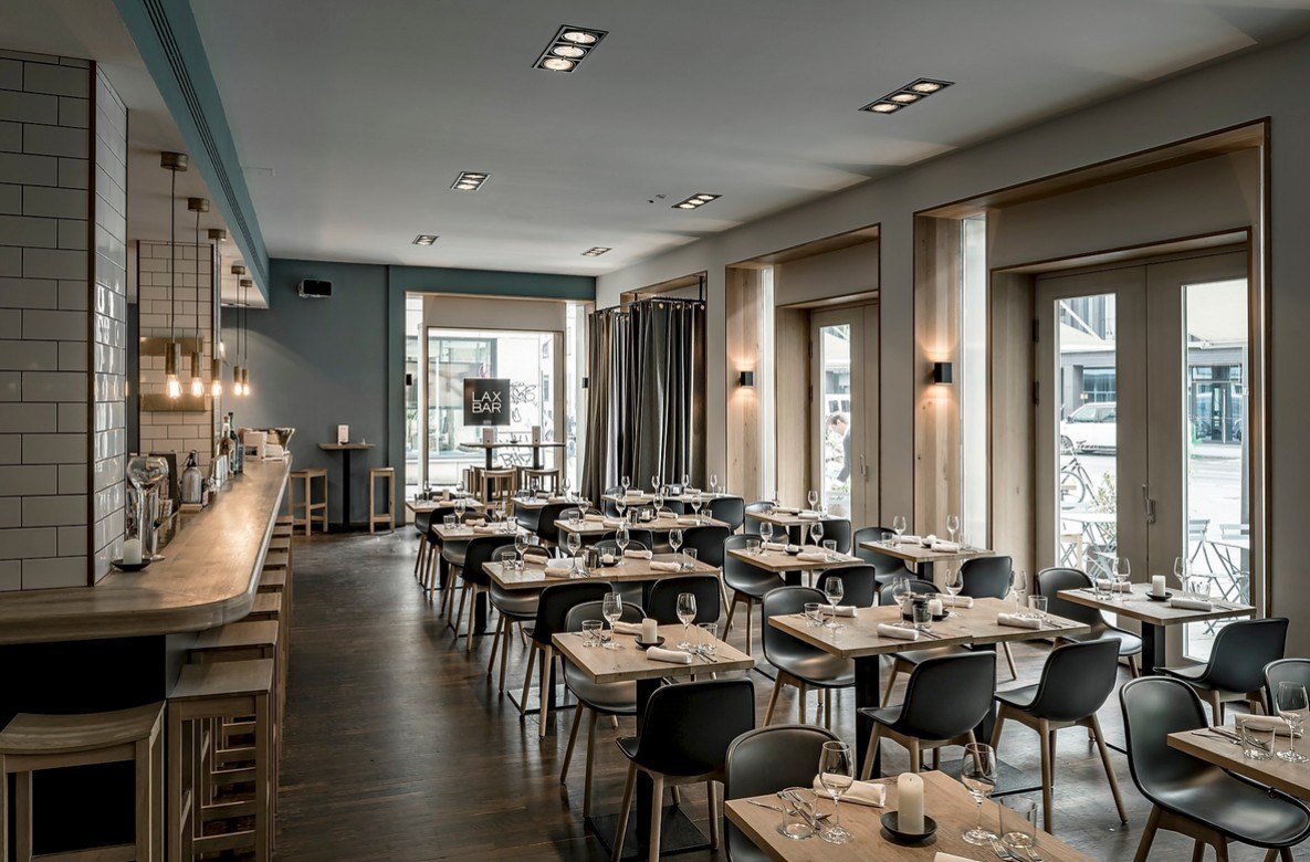 Heller Restaurantraum mit Bartheke, Holztischen und schwarzen Stühlen im Tageslicht