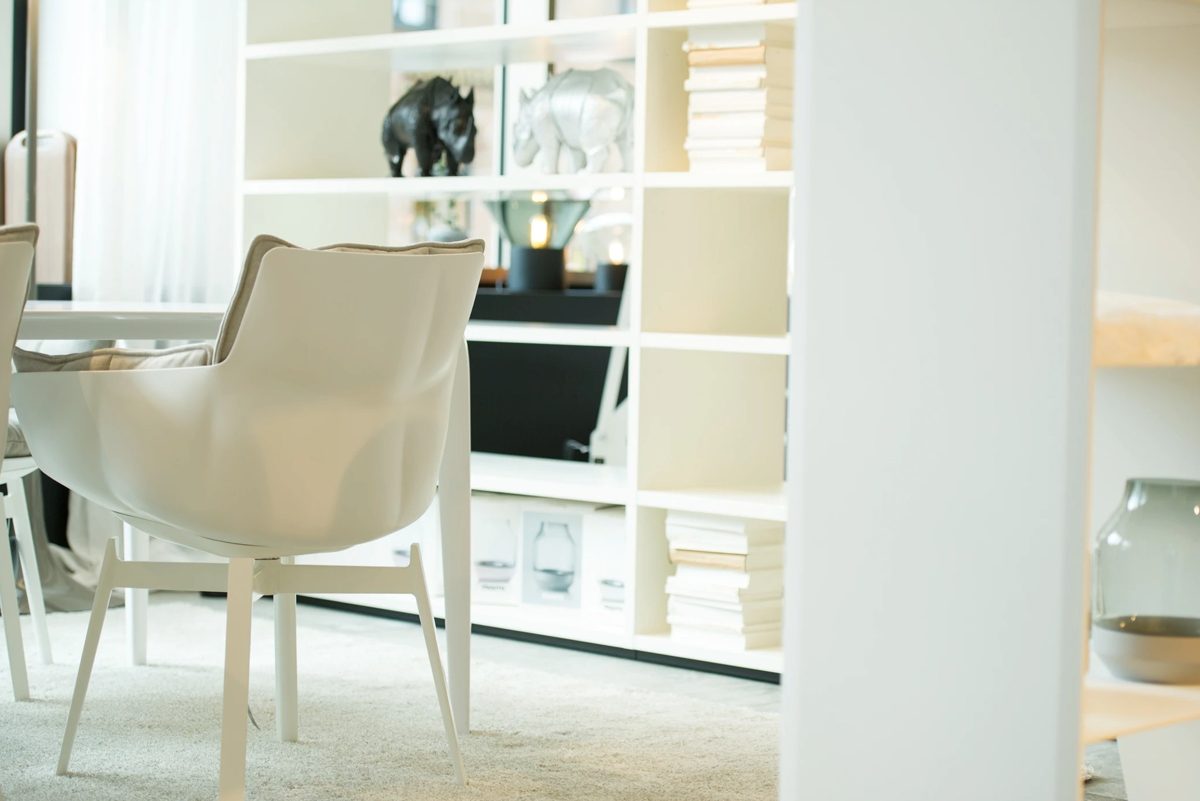 Weißer Schalensessel vor einer hellen Regalwand mit Büchern und Dekoobjekten