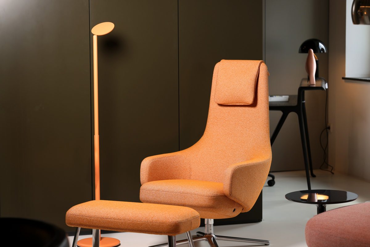 Oranger Designsessel mit Hocker und Stehleuchte vor dunkelgrüner Schrankwand