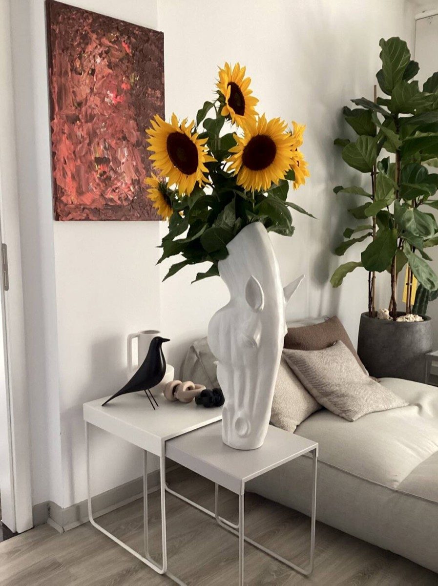 Wohnzimmerecke mit heller Couch, Designvase mit Sonnenblumen und abstraktem Wandbild