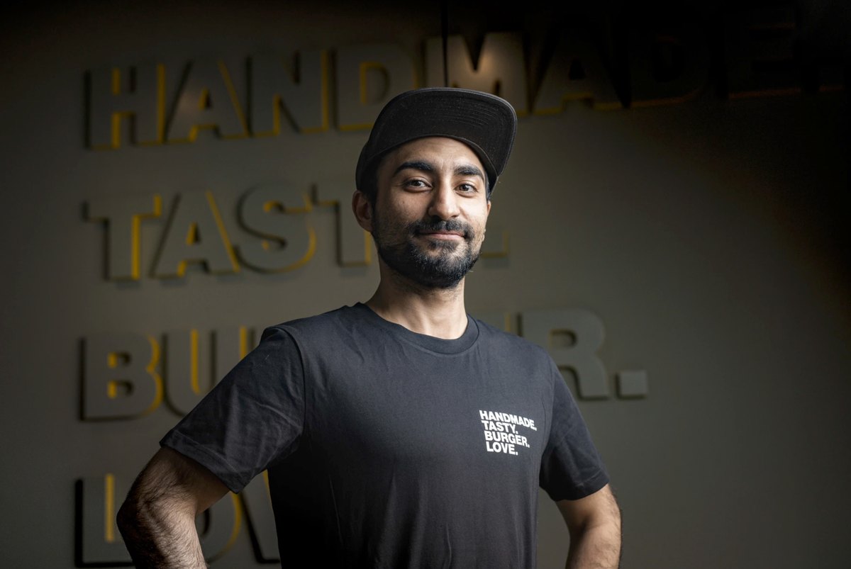 Barista im Portrait vor beleuchtetem Schriftzug an der Wand