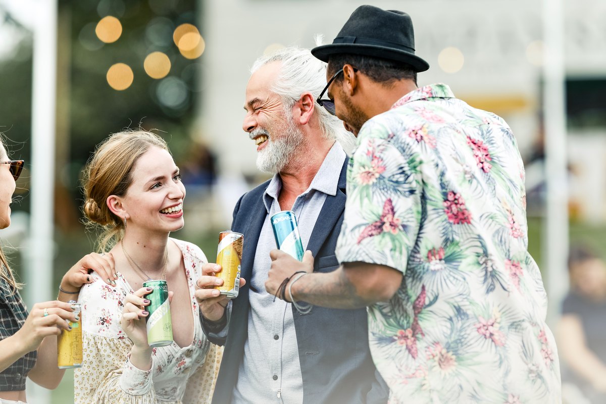 Freunde stossen im Abendlicht eines Festivals mit Getränkedosen an