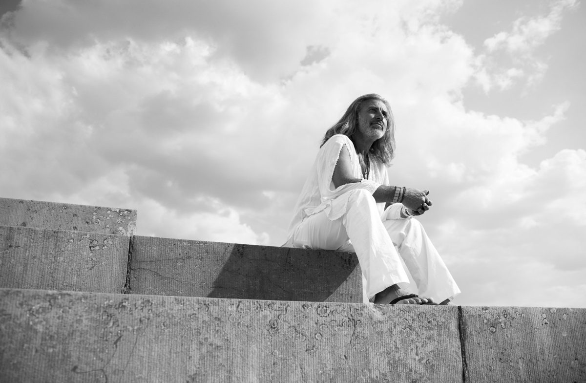 Frau in weißer Kleidung sitzt auf einer Betonmauer vor großem Wolkenhimmel in Schwarzweiss