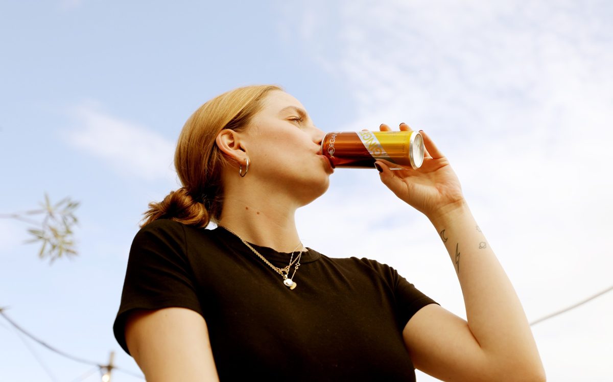 Frau trinkt aus einer Dose vor blauem Sommerhimmel