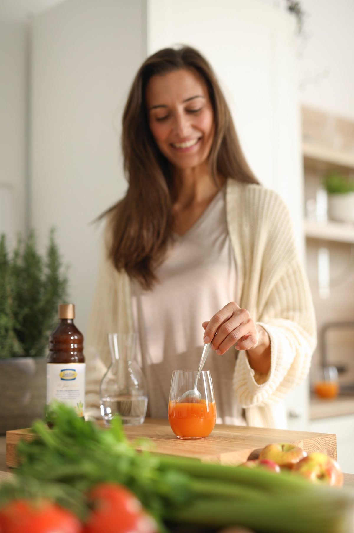 Frau rührt in einer hellen Küche ein Glas mit orangefarbenem Saft an