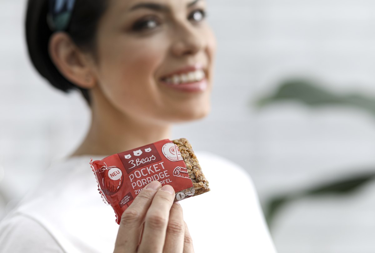 Lächelnde Frau hält einen verpackten Snackriegel in die Kamera