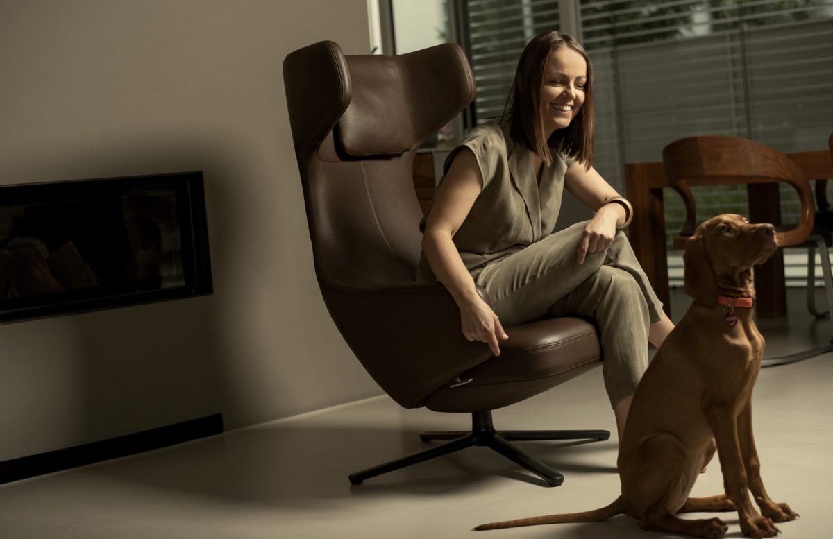 Lifestyleportrait einer Frau im Sessel mit ihrem Hund in einem modernen Wohnraum
