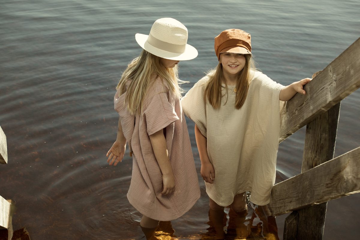 Zwei Kinder in Musselin-Ponchos stehen im flachen Wasser eines Sees im warmen Abendlicht