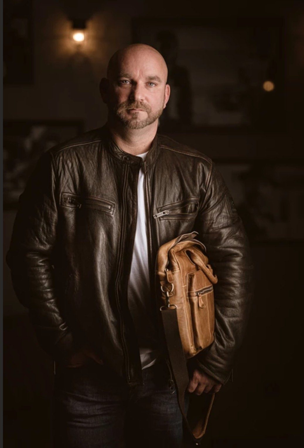 Mann in brauner Lederjacke mit Ledertasche unter dem Arm in warm beleuchtetem Raum