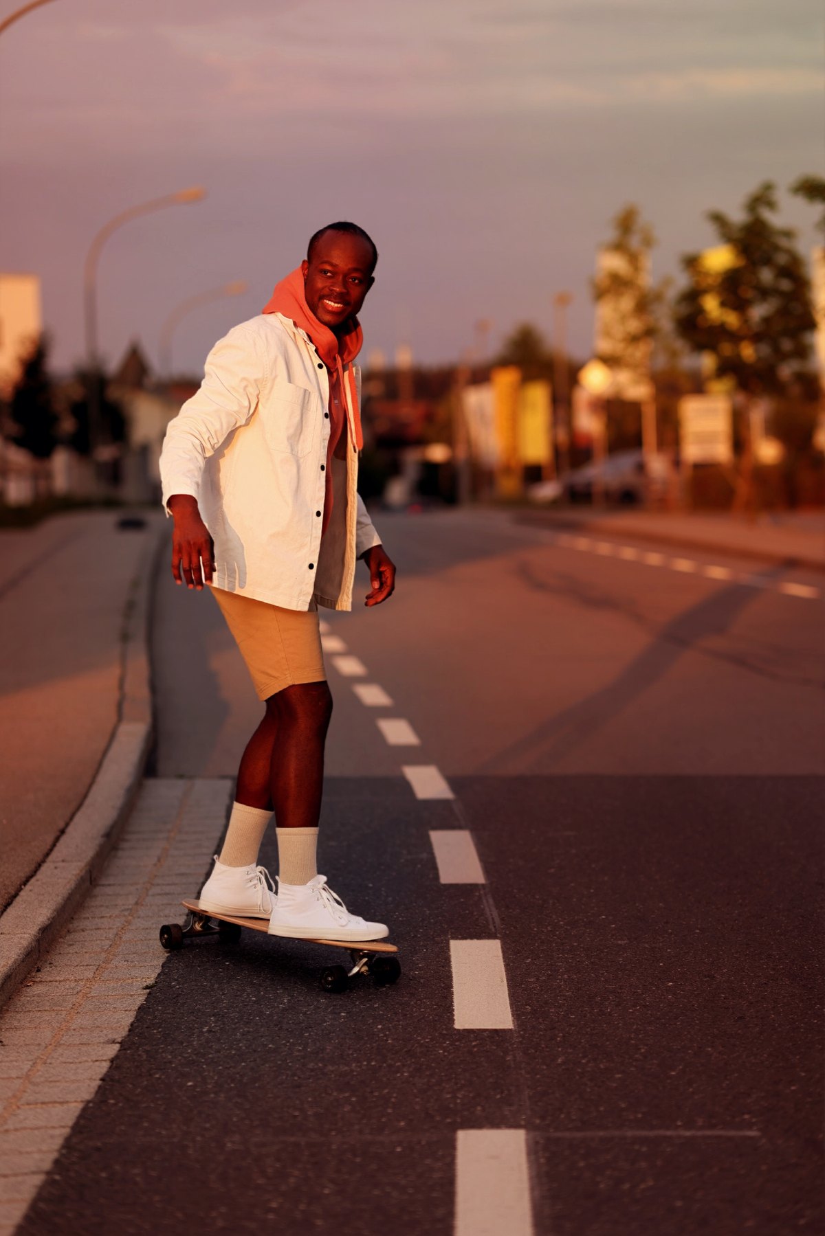 Lachender Mann fährt Longboard auf einer Straße im warmen Abendlicht