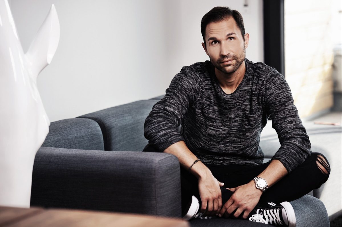 Mann im melierten Pullover sitzt auf einem grauen Sofa in hellem Wohnraum