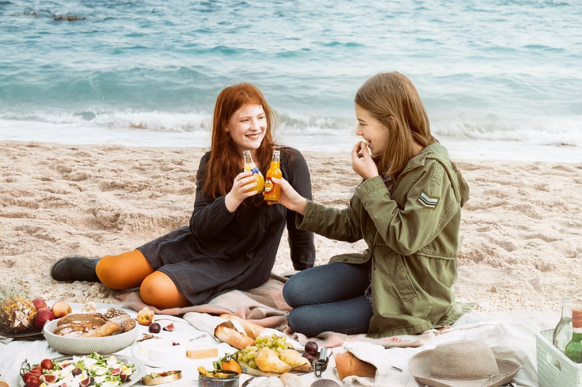 Zwei Frauen beim Picknick am Strand stossen mit Flaschen an