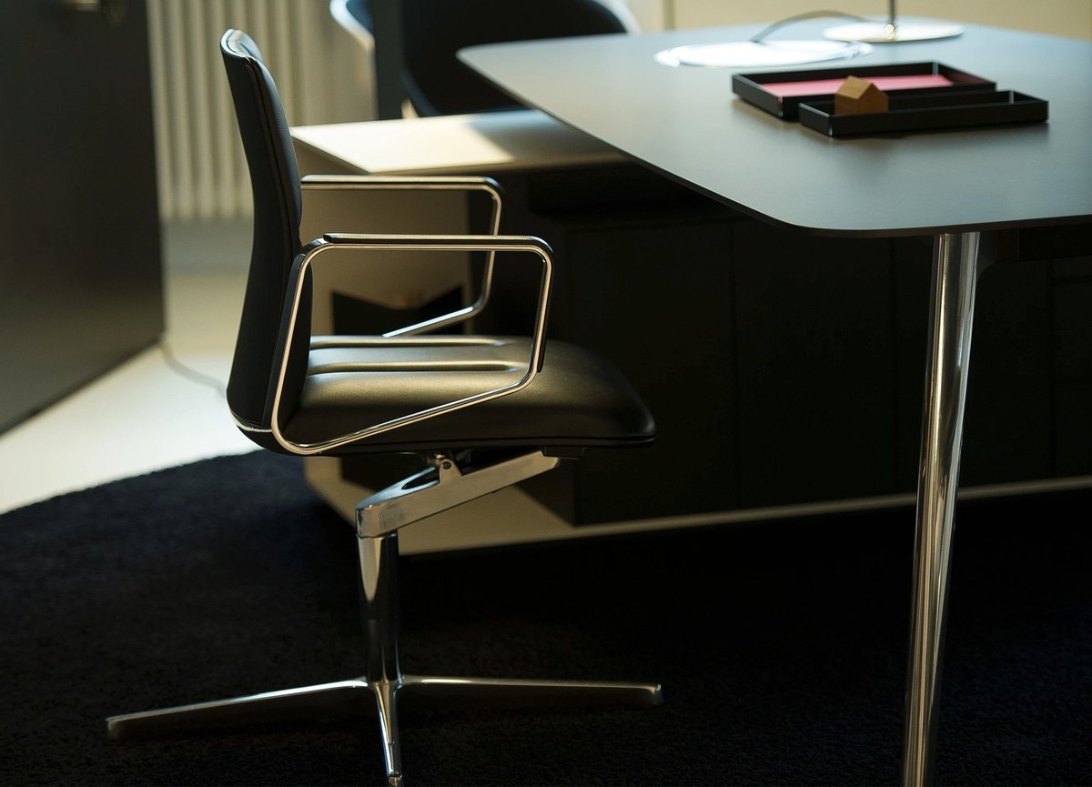 Schwarzer Lederdrehstuhl an einem Schreibtisch in dunklem Büroambiente
